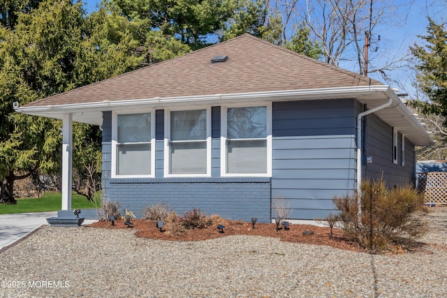 view of side of home featuring brick siding and a shingled roof