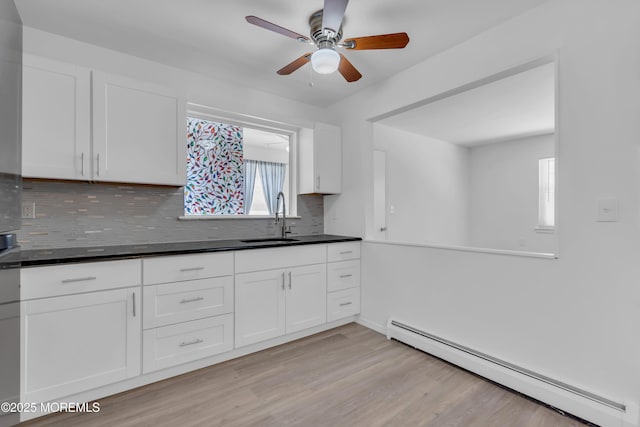 kitchen with a sink, backsplash, white cabinets, baseboard heating, and ceiling fan