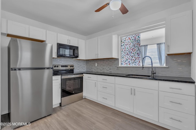 kitchen with light wood-type flooring, a sink, dark countertops, stainless steel appliances, and white cabinets