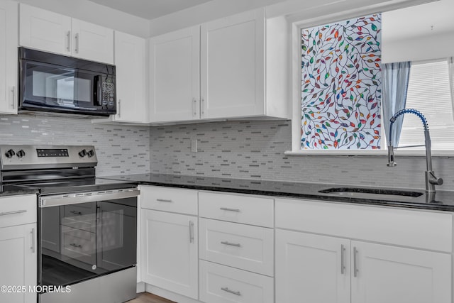 kitchen with stainless steel electric range oven, dark stone countertops, a sink, white cabinets, and black microwave