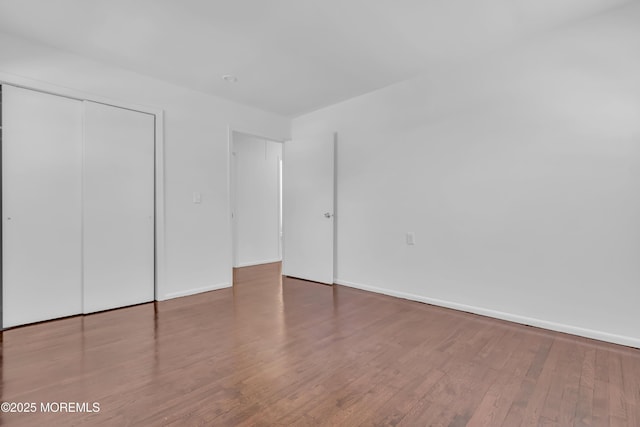 unfurnished bedroom featuring wood finished floors, a closet, and baseboards