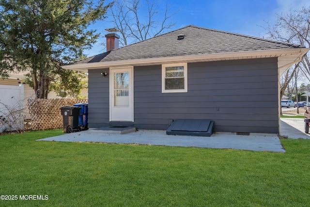 rear view of house featuring a shingled roof, fence, a lawn, a chimney, and a patio area