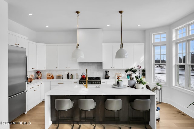 kitchen with visible vents, a breakfast bar area, decorative backsplash, light wood-style flooring, and built in fridge