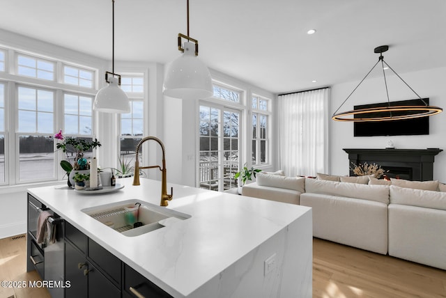 kitchen with a sink, a kitchen island with sink, dark cabinetry, and light wood finished floors