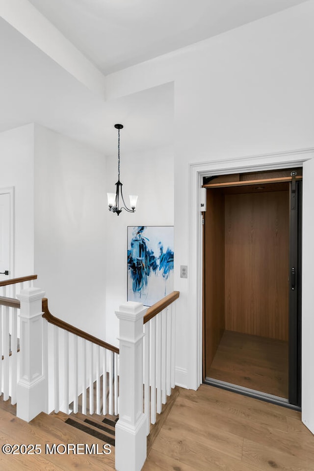 hall featuring elevator, a notable chandelier, an upstairs landing, and light wood-style floors