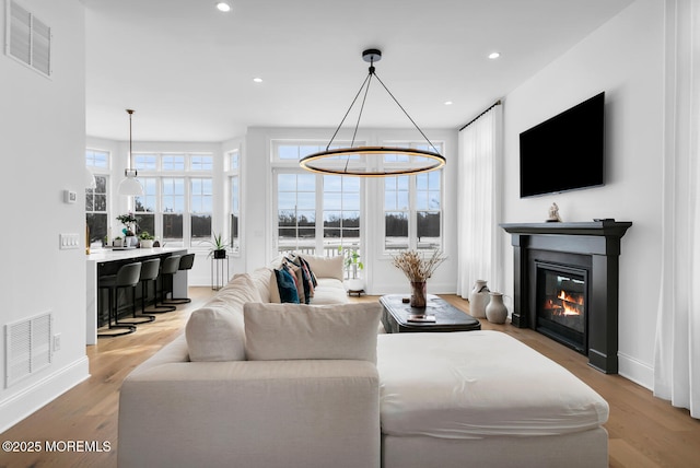 living area with a glass covered fireplace, recessed lighting, wood finished floors, and visible vents