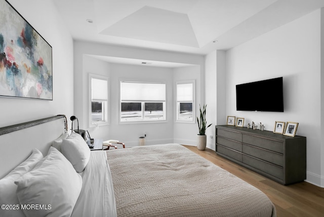 bedroom with a tray ceiling, wood finished floors, and baseboards