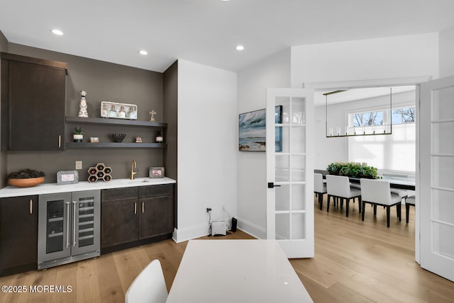 interior space featuring beverage cooler, dark brown cabinets, light wood finished floors, and a sink