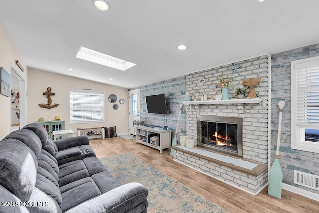 living room featuring a brick fireplace, baseboards, recessed lighting, a skylight, and wood finished floors