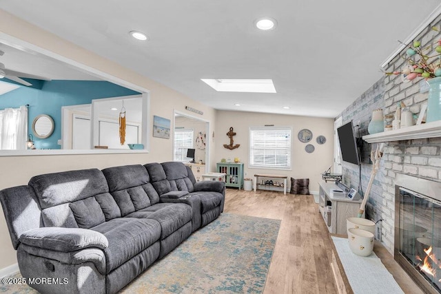 living room featuring lofted ceiling with skylight, wood finished floors, recessed lighting, a fireplace, and baseboards