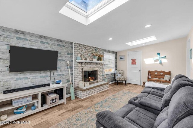 living room with a brick fireplace, an accent wall, recessed lighting, a skylight, and wood finished floors