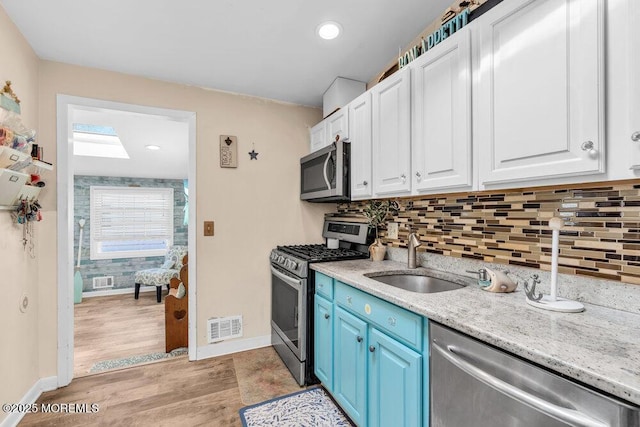 kitchen featuring visible vents, a sink, appliances with stainless steel finishes, white cabinetry, and light wood-type flooring