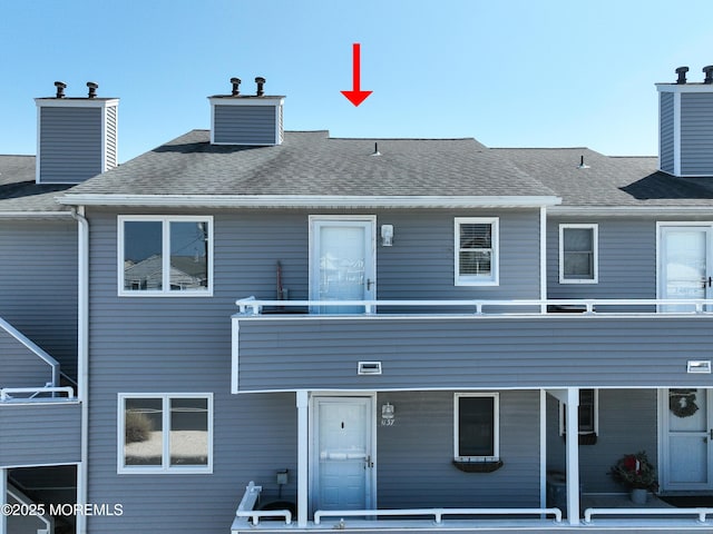 rear view of house with a chimney, a balcony, and roof with shingles