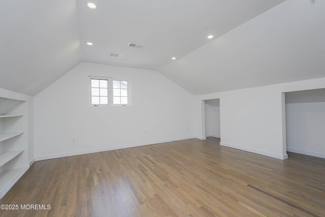 bonus room featuring built in features, baseboards, wood finished floors, and vaulted ceiling