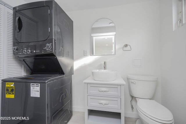 bathroom with vanity, toilet, baseboards, and stacked washer and clothes dryer