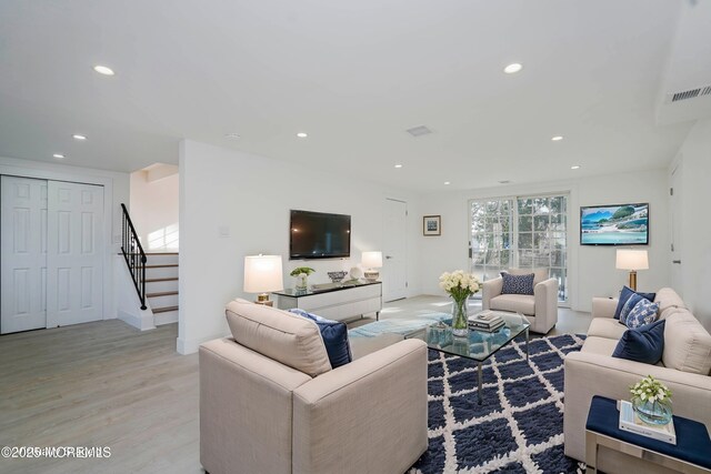 living room featuring light wood-style flooring, visible vents, recessed lighting, and stairs