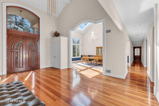 entrance foyer with visible vents, a notable chandelier, high vaulted ceiling, light wood-style floors, and baseboards