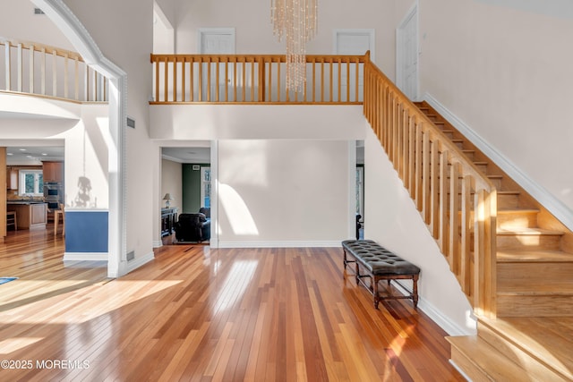 stairway with an inviting chandelier, a towering ceiling, baseboards, and wood-type flooring