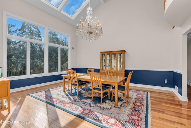 dining space with a notable chandelier, baseboards, high vaulted ceiling, and wood finished floors