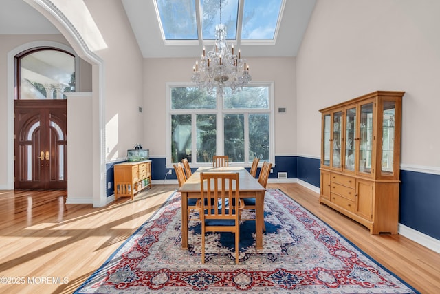 dining room with baseboards, a skylight, an inviting chandelier, wood finished floors, and high vaulted ceiling