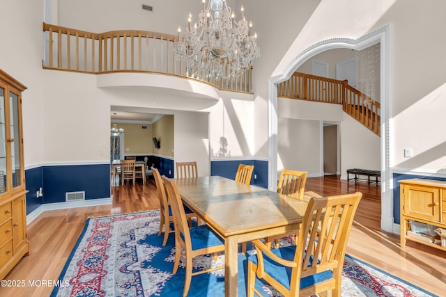 dining area with visible vents, light wood-type flooring, a towering ceiling, and a chandelier