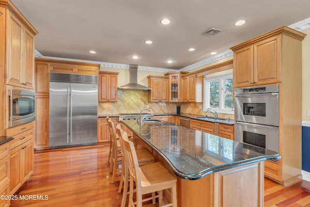 kitchen featuring a kitchen bar, wall chimney exhaust hood, light wood-type flooring, and built in appliances