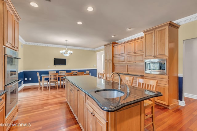 kitchen featuring an inviting chandelier, an island with sink, a sink, appliances with stainless steel finishes, and light wood-type flooring