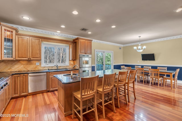 kitchen with visible vents, a notable chandelier, a breakfast bar, appliances with stainless steel finishes, and brown cabinetry