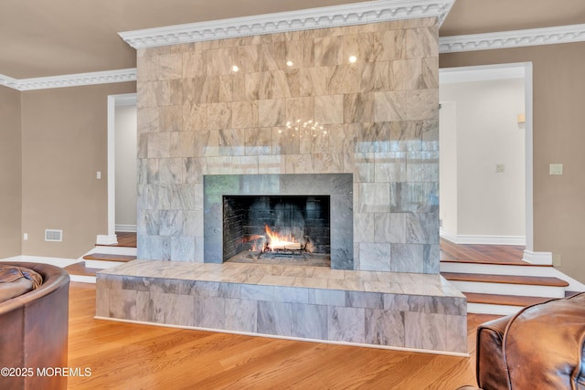 room details featuring visible vents, ornamental molding, a tiled fireplace, wood finished floors, and baseboards