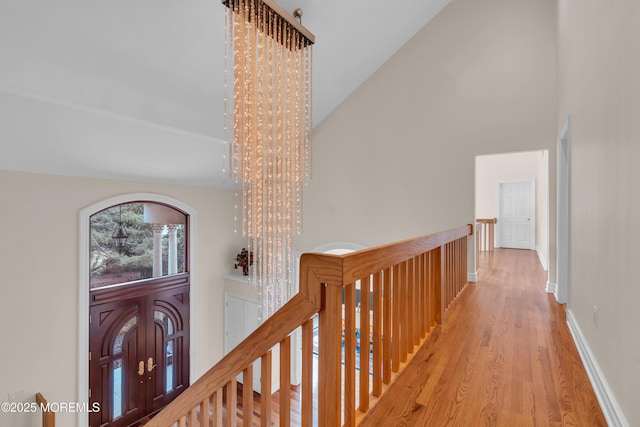 hallway featuring an upstairs landing, a notable chandelier, wood finished floors, and high vaulted ceiling