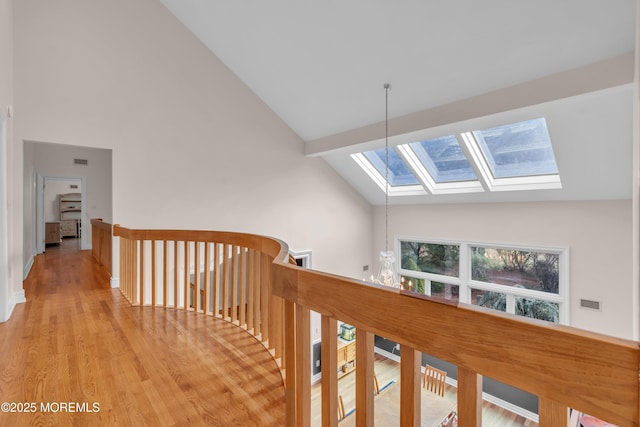 corridor featuring wood finished floors, high vaulted ceiling, a skylight, a notable chandelier, and an upstairs landing