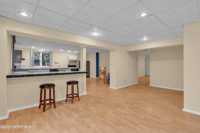 kitchen featuring dark countertops, a breakfast bar area, light wood-style flooring, and freestanding refrigerator