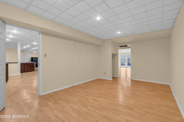 empty room with light wood finished floors, a paneled ceiling, and baseboards