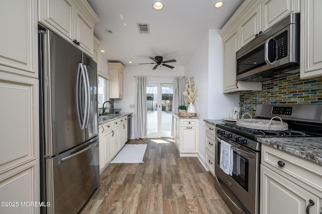 kitchen featuring backsplash, dark wood finished floors, light stone counters, stainless steel appliances, and a sink