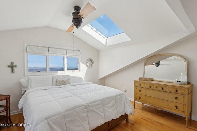 bedroom featuring vaulted ceiling with skylight, baseboards, a ceiling fan, and wood finished floors