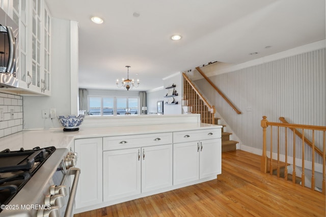 kitchen with a peninsula, white cabinetry, stainless steel range with gas cooktop, and light wood-style floors