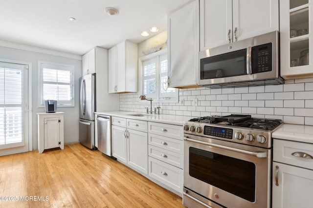 kitchen featuring tasteful backsplash, light wood finished floors, light countertops, appliances with stainless steel finishes, and a sink