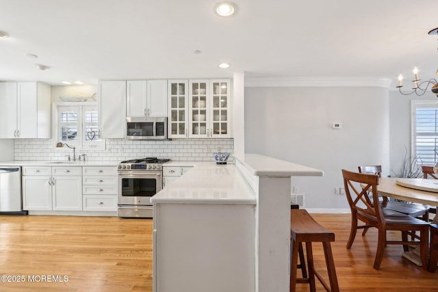 kitchen featuring a kitchen bar, backsplash, white cabinetry, appliances with stainless steel finishes, and light wood finished floors