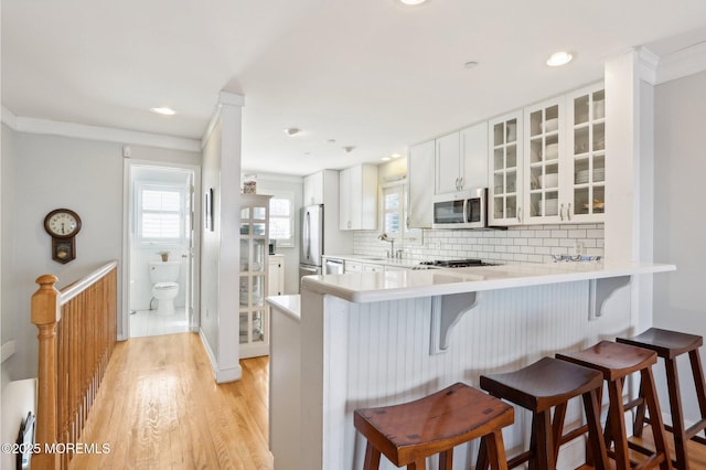 kitchen featuring stainless steel appliances, glass insert cabinets, a breakfast bar, and decorative backsplash