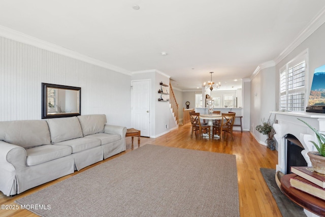 living room with crown molding, a chandelier, stairs, light wood-type flooring, and a fireplace