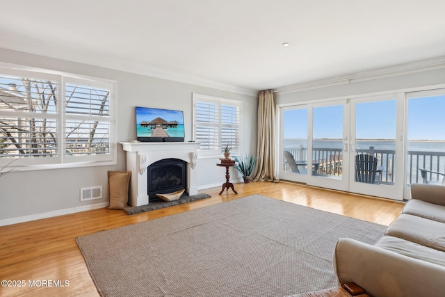 living room featuring visible vents, a fireplace with raised hearth, crown molding, baseboards, and wood finished floors