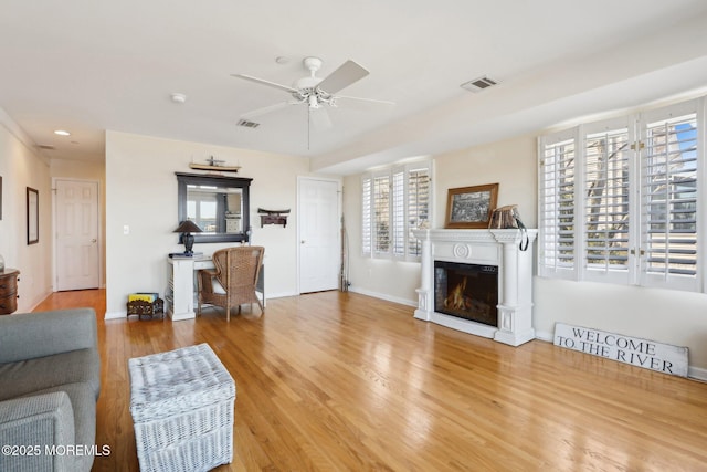 living area with visible vents, baseboards, wood finished floors, a glass covered fireplace, and a ceiling fan