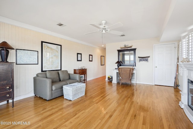 living room featuring a wealth of natural light, light wood-type flooring, visible vents, and a glass covered fireplace