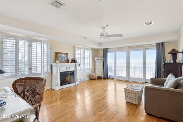 living area with a glass covered fireplace, wood finished floors, visible vents, and a ceiling fan