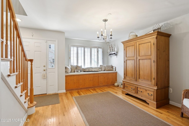 foyer entrance featuring stairs, baseboards, light wood finished floors, and a chandelier