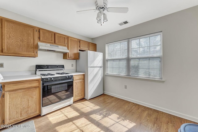 kitchen with visible vents, under cabinet range hood, range with gas stovetop, freestanding refrigerator, and light wood-style floors