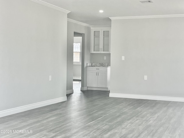 unfurnished living room with visible vents, baseboards, ornamental molding, wood finished floors, and a baseboard radiator