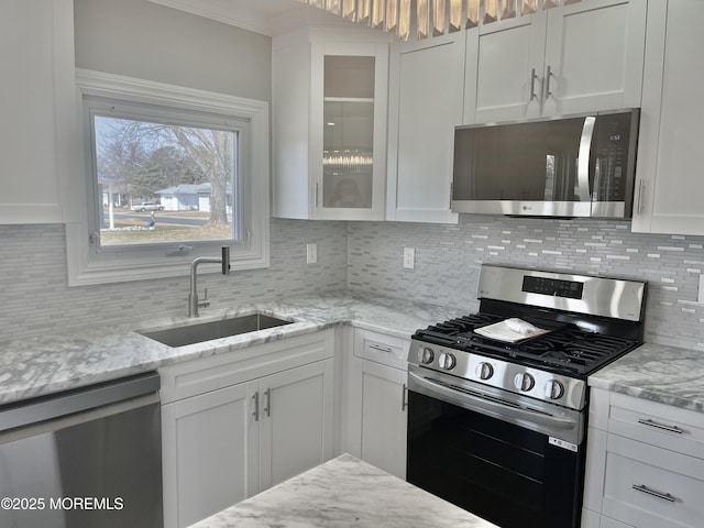 kitchen featuring glass insert cabinets, decorative backsplash, appliances with stainless steel finishes, white cabinetry, and a sink