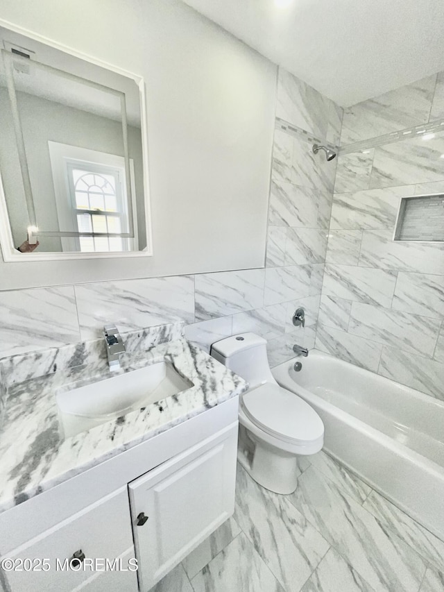 full bathroom with toilet, marble finish floor, tile walls, washtub / shower combination, and vanity