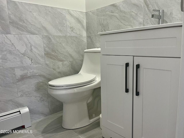 half bath featuring tile walls, baseboard heating, toilet, and vanity